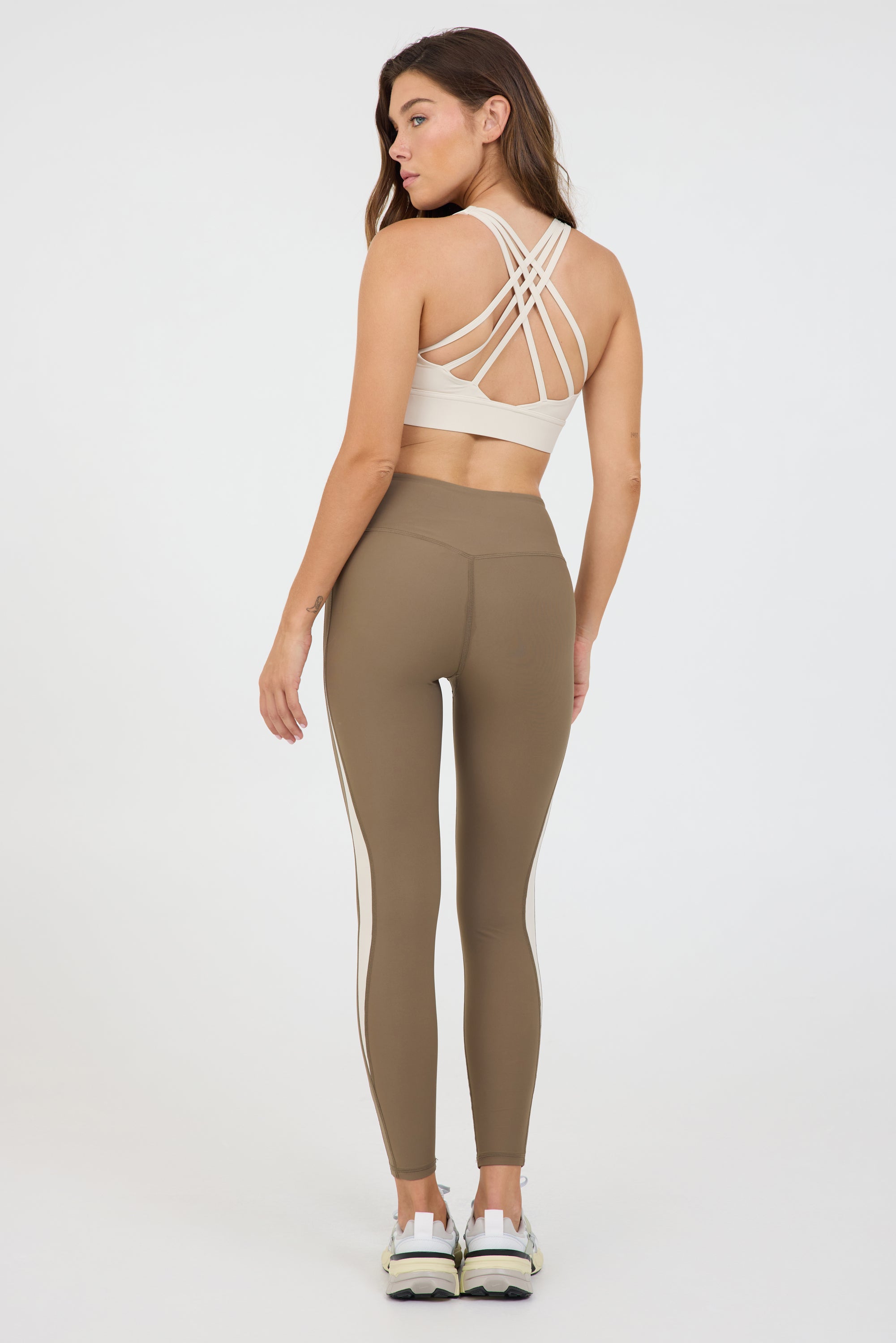 Carey strappy bra with removable bra cups in cream, modeled with the truffle and cream krista side panel 7/8 leggings from the back