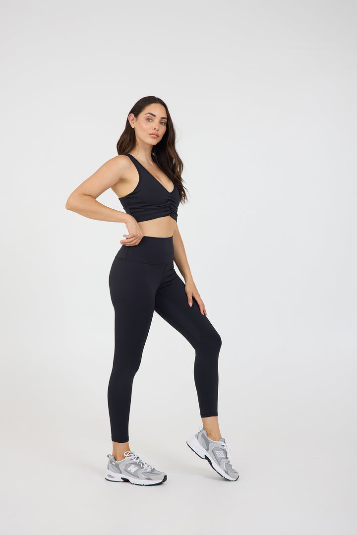 Julia Ruched front strapped bra in black, modeled with the Kenzie 7/8 leggings from the side
